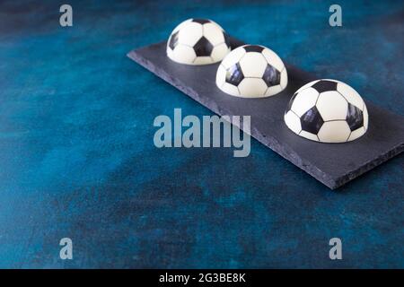 Three chocolate cakes in the shape of football balls on a rectangular black plate in the corner with copy space. A creative gift for a fan of european Stock Photo