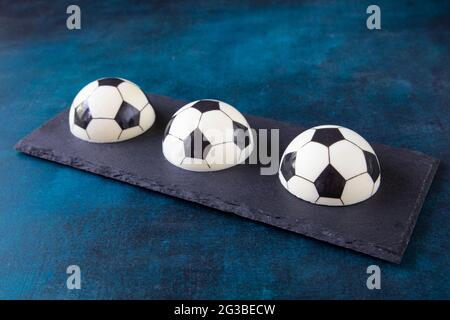 Delicious beautiful dessert in the shape of three halves of the ball - sweet cakes on a black serving board. Creative designer pastries for snacks whi Stock Photo