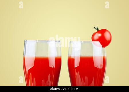 Two glasses with tomato juice and a small tomato on a yellow background. Stock Photo