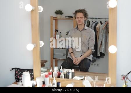 Young man with zombie greesepaint sitting in front of mirror in studio Stock Photo