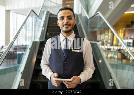 Young hotel manager with tablet standing in front of escalator Stock Photo