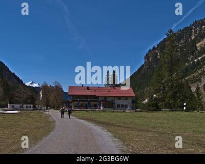 Hikers passing the mountain guesthouse Berggasthof Oytalhaus in Oytal valley, Allgeau, Alps on sunny day in early summer with blue sky. Stock Photo