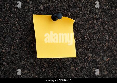 A blank yellow paper note pinned to a brown cork board. Close up. Stock Photo