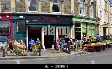 Restaurant with customers eating outside on pavement and fruit and veg store with produce on display outside Stock Photo
