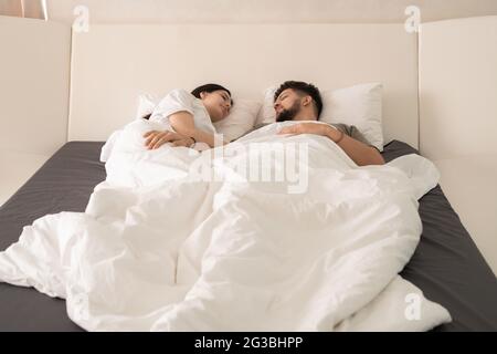 Contemporary young just married couple sleeping under white blanket Stock Photo