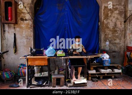 A woman uses a sewing machine at her outdoor tailor shop located in a narrow alley  in Chinatown, Bangkok, Thailand Stock Photo