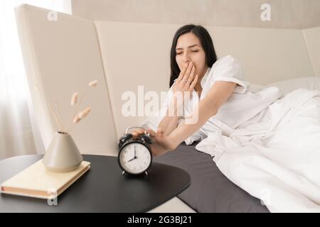 Girl stopping alarm clock and yawning after sleep Stock Photo