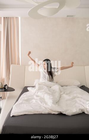 Happy young woman stretching arms in bed after sleep Stock Photo