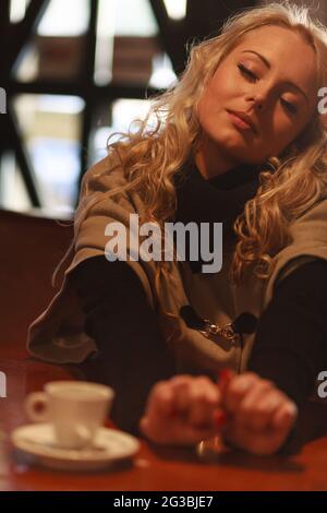 Young woman relaxing indoors with a hot cup of coffee stretching her arms across the table with a smile of pleasure in a close up portrait Stock Photo