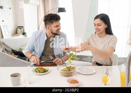 Young woman putting vegetable salad on plates during breakfast Stock Photo