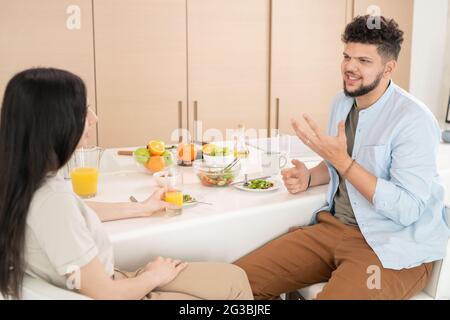 Young couple talking by breakfast while sitting by kitchen table Stock Photo