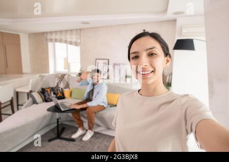Happy female making selfie with her husband on background in home environment Stock Photo