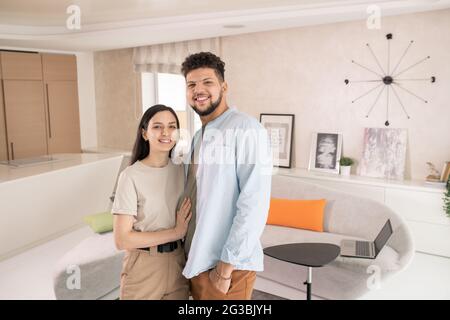 Happy young couple standing in front of camera in living-room Stock Photo