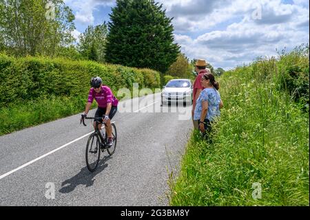 A group of ramblers standing on the grass verge while cycle and car go past along South Road between Plumpton Green and South Chailey, East Sussex, En Stock Photo