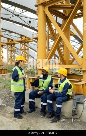 Three intercultural workers in uniform having tea with sandwiches at lunch break Stock Photo