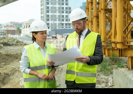 Young female engineer listening to colleague explaining sketch on blueprint Stock Photo