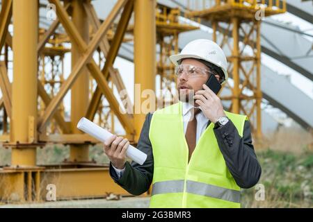 Young engineer in workwear talking on the phone on construction site Stock Photo