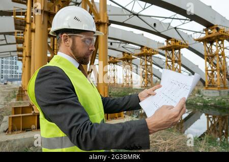 Young serious builder looking at sketch on paper while working Stock Photo