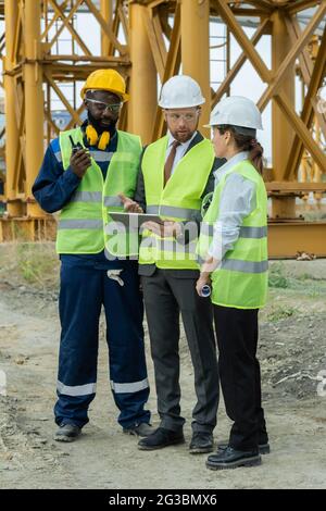 Group of builders discussing sketch on tablet screen at construction site Stock Photo