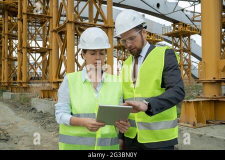 Two confident builders in workwear using digital tablet during discussion of working points Stock Photo