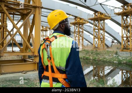 Young African engineer standing on construction site and looking at huge frames Stock Photo