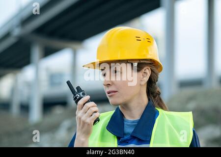 Female inspector or engineer using walkie-talkie while working on construction site Stock Photo