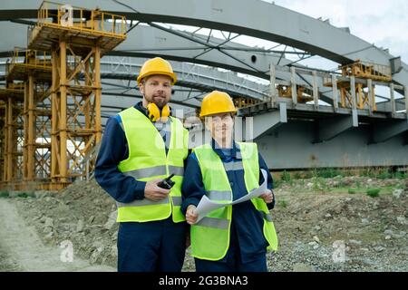 Two successful engineers in workwear standing against large construction frame Stock Photo