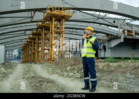 Contemporary builder using walkie-talkie against huge construction frame Stock Photo
