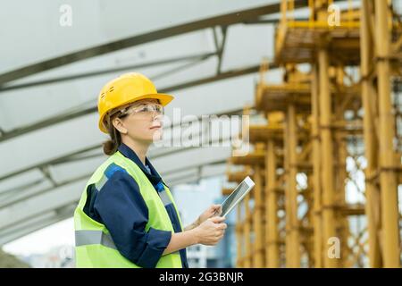 Happy female engineer with tablet looking at huge construction frame Stock Photo