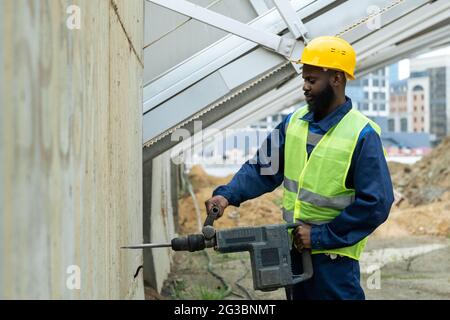 Young African builder drilling concrete wall with huge drill Stock Photo
