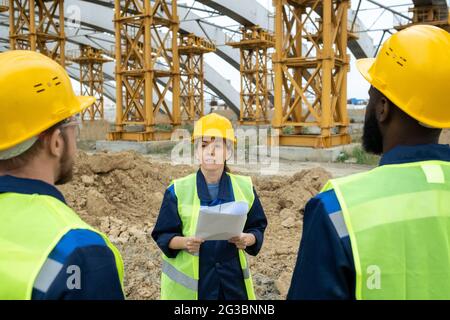 Female engineer in workear talking to her male colleagues at meeting Stock Photo