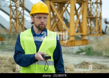 Young builder in uniform and protective helmet and eyeglasses using work tool Stock Photo