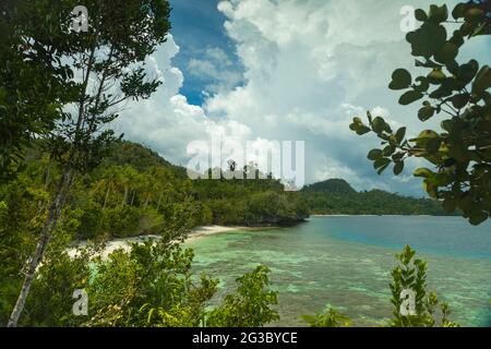 Huge storm clouds loom over the green landscape of beaches and rainforests, on the island of Gam, in Raja Ampat, West Papua, Indonesia Stock Photo