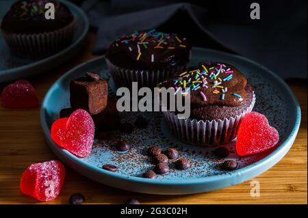 Valentinesday cupcake. Tasty chocolate cupcakes with cream and colored sprinkles. Sweet delicious dessert truffle and heart shaped candy on a plate. D Stock Photo