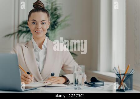 Young successful female freelancer writing down information in notepad Stock Photo