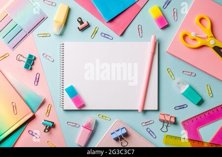 Creative student desk with white sheet of notebook paper and school supplies. Top view with copy space. Back to school flat lay on blue and pink background Stock Photo