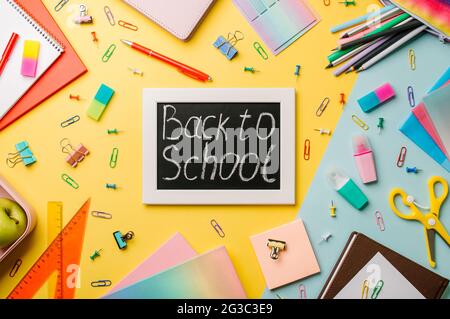 Blackboard with letters back to school made with chalk and stationery, school supplies on yellow and blue background. Top view or flat lay. Back to school concept Stock Photo