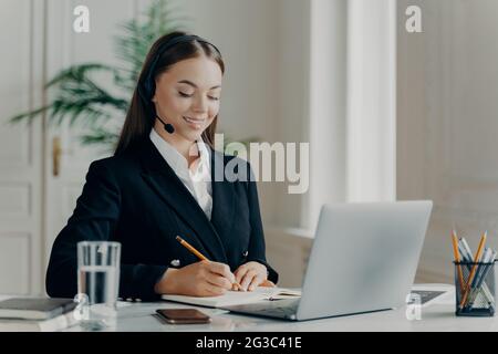 Smiling young businesswoman looking down and writing notes Stock Photo