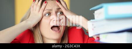 Woman holding her head and is surprised in front of many folders on table Stock Photo