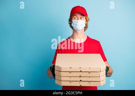 Photo of young guy hold carton pizza boxes look empty space wear face safe mask isolated on blue color background Stock Photo