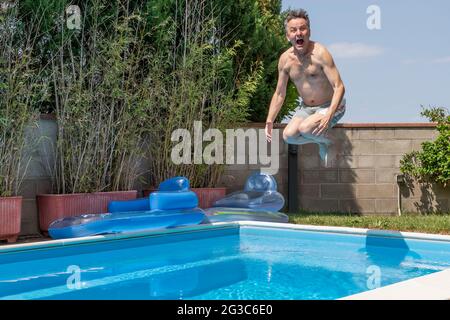 White man with a funny expression takes a cannon ball dive in a swimming pool on a sunny day Stock Photo