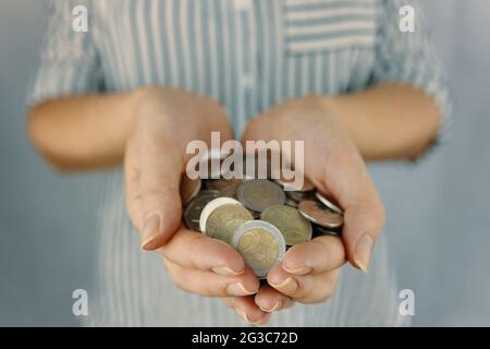 Woman holds coins in hands. Female in striped shirt with finances. Concept of savings. Handful of coins. Stock Photo