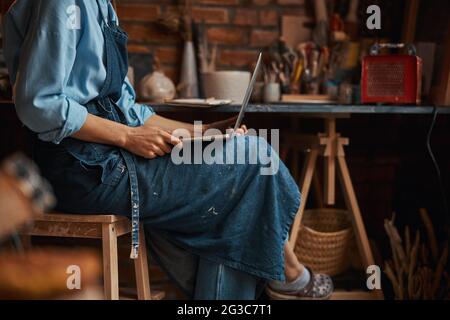 Beautiful elegant young sculptor spending time in pottery workshop while using internet in pottery workshop Stock Photo