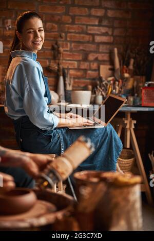 Young Caucasian female sculptor working in art studio while using internet Stock Photo