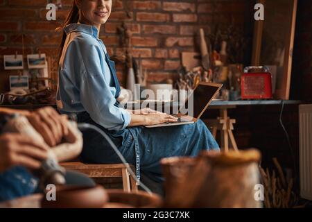 Happy smiling unrecognized woman in apron spending time in pottery workshop Stock Photo