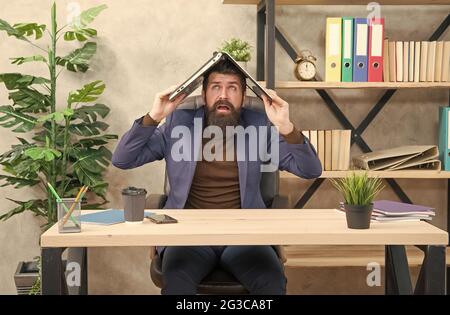 Crazy trader in formalwear hold notebook computer on head sitting at desk in business office, e-commerce Stock Photo