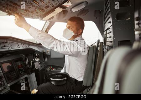 Male pilot turning button on passenger airplane Stock Photo