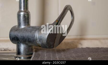 An old single lever valve with a leak. Chrome-plated basin mixer with running water on the basin Stock Photo