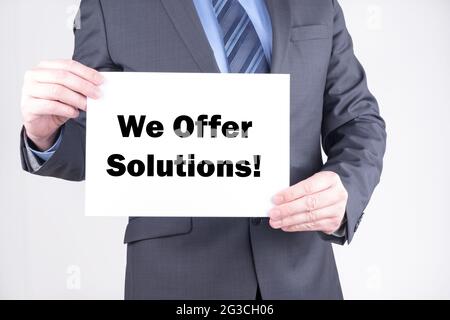 Man in a suit showing a paper sign with the text "we offer solutions" Stock Photo
