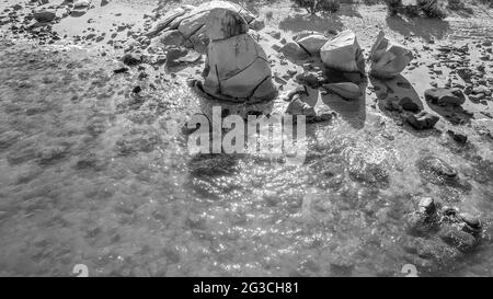 Aerial of a tall rock formation on the beach at low tide, rendered in black and white Stock Photo